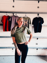 Load image into Gallery viewer, Model wearing olive green 85th Bike Week 2026 Main Street Station cropped t-shirt with small front chest logo in Daytona Beach.
